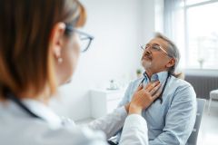 A senior man describes chest pain to a female doctor during a medical consultation. The scene depicts a healthcare setting with neutral tones and focuses on patient care and health concerns. A concerned expression and hand gesture highlight the discomfort.