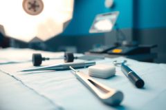 Surgical instruments on a sterile blue drape. Includes forceps, scissors, and a gauze pad, suggesting a medical or operating room setting. Close-up shot with shallow depth of field.