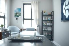 Spa room interior. A treatment table with products on a tray, black shelves with toiletries, and a relaxing environment. Natural light, modern design, calming blue tones.