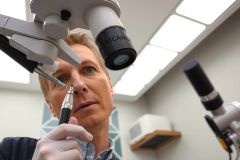 Scientist in lab coat examining a sample under a microscope, wearing gloves. Close-up view in a bright, modern research environment. Focus on precision and scientific analysis.
