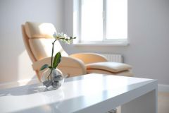Modern interior featuring a comfortable armchair, a white table with a potted orchid, and soft natural light. The scene evokes a sense of relaxation and tranquility, showcasing a stylish home decor.