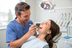 Dentist examines a patient's teeth in a bright dental operatory as the patient smiles during exam.