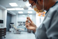 Doctor in scrubs holds a syringe in a brightly lit medical office. Focus on healthcare, medical professional, and clinical environment. Sterile and clean setting.