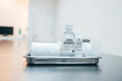 Hotel amenities on a silver tray. Includes a shampoo bottle, conditioner, and rolled towels. Clean, modern bathroom setting with a gray color scheme.