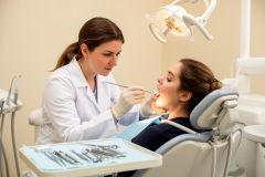 Dentist examining a patient's open mouth under an operatory light during a routine gum and teeth check.