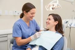 Dentist in blue scrubs smiling and speaking with a relaxed patient seated in a dental chair.