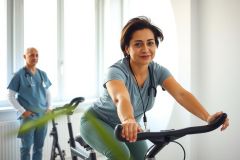 Woman on exercise bike in a clinic setting, monitored by a doctor. Healthcare, fitness, patient recovery, rehabilitation, medical check-up, and wellness themes are present.