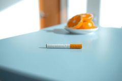 Close-up of sliced oranges in a white bowl on a blue surface. A cigarette lies nearby, creating a still life composition with vibrant colors and a casual, slightly melancholic atmosphere.