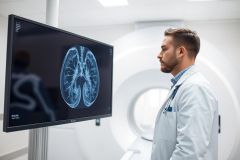 Doctor examining a brain MRI scan on a monitor in a modern medical facility. The image displays blue and white tones, highlighting neurological imaging and diagnostic technology. Healthcare professional, medical imaging, radiology.