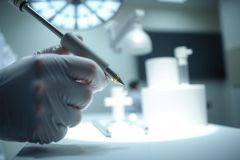 Close-up of a hand wearing a white glove holding a tool, likely for precision work. The image showcases a clean, bright environment with a focus on detail and accuracy, potentially a laboratory or jewelry setting.
