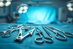 Surgical instruments laid out on a sterile blue operating table in a modern operating room. Focus is on stainless steel tools including scissors and forceps, with bright overhead surgical lights in the background. Medical equipment, healthcare, and surgical theme.