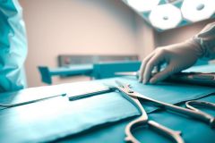 Surgical instruments and a gloved hand on a blue operating table in a sterile environment. Close-up view of medical tools in a hospital setting.