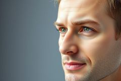 Close-up portrait of a man with blue eyes and a slight beard. The background is a blurred, dark grey. Focused on facial features and capturing a contemplative expression. Ideal for portraits, men's style, or blue eye imagery.