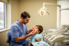 Dentist gently examines a young boy's mouth in a pediatric dental exam room, reassuring the child.
