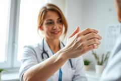 A smiling female doctor in a white coat consults with a patient in a bright, modern clinic. The image conveys healthcare, medical consultation, and patient care with a focus on a friendly doctor-patient relationship. Warm, natural lighting and a clean environment enhance the professional atmosphere.