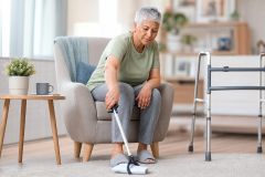 Older adult using a reacher to pick up cloth at home, walker nearby for hip replacement recovery.