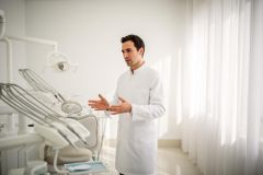 Dentist in a bright dental operatory explaining treatment, hands gesturing as he speaks.