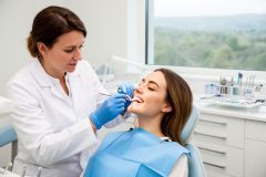 Dentist examining a smiling young woman's teeth in a bright, modern dental treatment room.