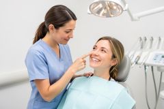 Dentist in scrubs smiling at a seated patient reviewing her smile in a dental operatory.