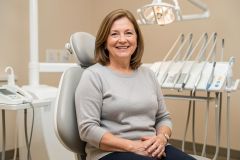 Smiling mature woman seated in a dental chair, suggesting a consultation about tooth replacement options.