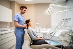 Dental clinician adjusting a patient's headrest as they discuss treatment in a modern operatory, patient reclining calmly.