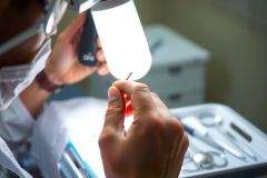 Close-up of a person in surgical attire examining something with a magnifying glass. Likely a medical or lab setting, focusing on precision and detail.