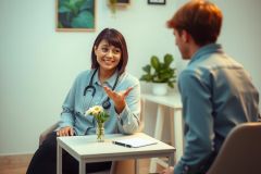 Doctor consults patient in a bright, modern office setting. Wearing a stethoscope, the doctor speaks with a concerned expression. Natural light and greenery create a calming atmosphere.