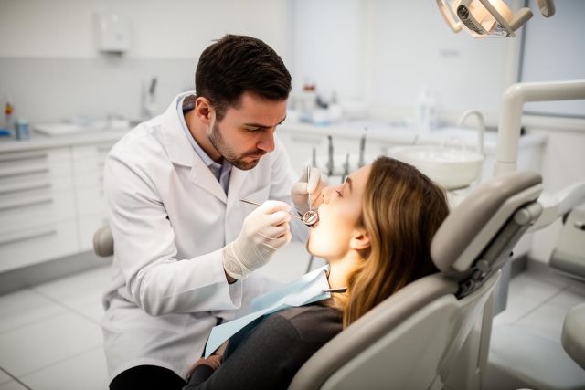 Dentist examining a patient's open mouth during a dental exam, inspecting teeth for restorations.