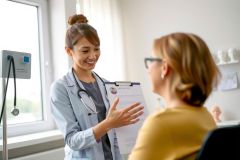 Doctor examining patient in clinic, holding clipboard. Healthcare professional consultation, medical checkup, patient care, doctor-patient relationship, clinical setting.