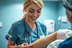 Nurse checking patient's arm bandage in a medical setting. Blue scrubs, stethoscope, and a focus on healthcare examination. Clean, bright environment.