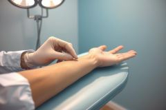 Medical professional in gloves administering an injection on a patient's arm. Blue medical environment with visible equipment. Healthcare procedure, close-up shot.