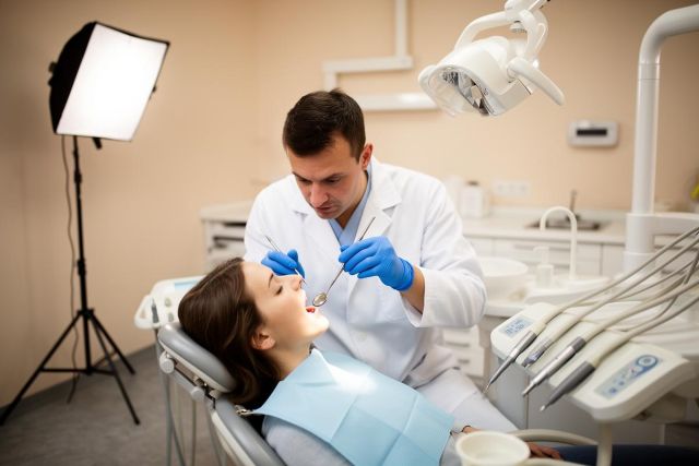 Dentist in gloves inspecting a patient's open mouth in a dental chair, preparing for restorative care.