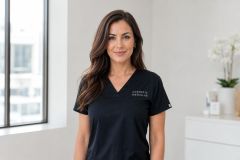 Clinician in cosmetic medicine scrubs standing in a bright, calm consultation room, approachable and professional.