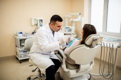 Dentist examining a patient in a dental chair, discussing orthodontic treatment while holding a mirror.