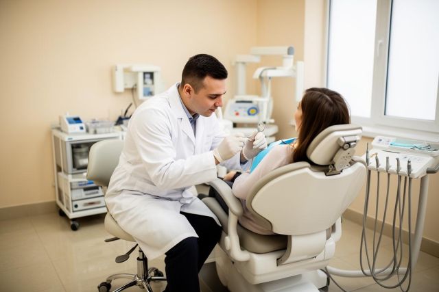 Dentist examining a patient in a dental chair, discussing orthodontic treatment while holding a mirror.