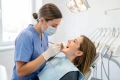 Dentist in blue scrubs examines a patient's teeth with a dental mirror and explorer during a routine visit.