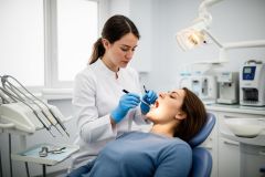Dentist in gloves examining a patient's open mouth with a mirror and probe during an oral assessment in clinic.