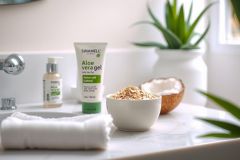 Close-up of skincare products on a white bathroom counter. Includes aloe vera gel, a white bowl with granules, a small bottle, and a rolled towel. Natural, clean, and spa-like aesthetic.