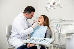 Dentist examining a woman's teeth in a dental chair during a cosmetic dental visit.