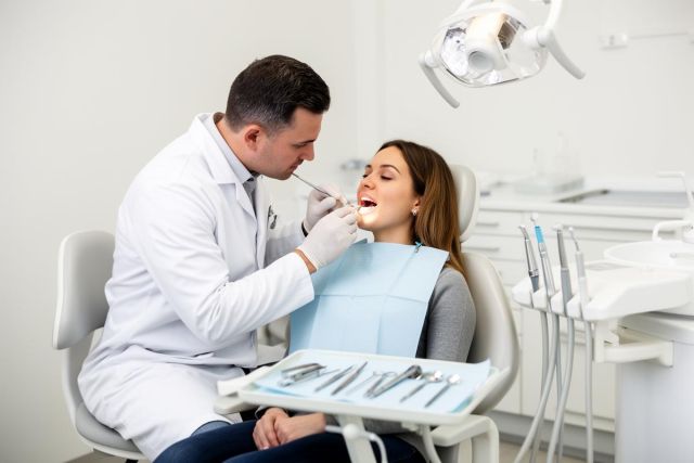 Dentist examining a woman's teeth in a dental chair during a cosmetic dental visit.