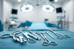 Surgical instruments arranged on a blue operating table in a blurred operating room setting. Surgical tools, medical equipment, and bright overhead lights create a sterile environment. Focus is on precision and healthcare.