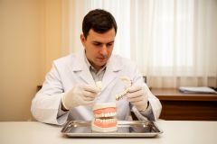 Dentist in gloves comparing a single dental crown and a multi-tooth bridge above a dental model.