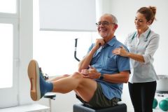 Physical therapy session. A therapist examines a patient seated on an elevated bench, assessing posture and mobility. Healthcare setting with exercise equipment in background.
