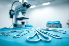 Surgical instruments laid out on a blue sterile drape, with a surgical microscope in the background. A clean, modern operating room setting. Focus on precision and medical equipment.