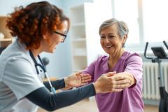 A healthcare professional and senior woman shake hands in a medical setting. The scene depicts a positive patient-doctor interaction, likely in a clinic or rehabilitation center. Warm colors and a friendly atmosphere are present.