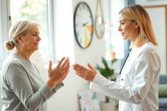 A healthcare professional, wearing a white coat and stethoscope, interacts with an older woman in a bright, modern home setting. The scene conveys care and well-being, featuring warm lighting and a friendly atmosphere.