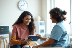 Doctor shows patient tablet in exam room. Healthcare professional consults with a patient in a brightly lit medical setting. Focus on patient care and digital health technology.