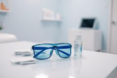 Blue light glasses and contact lens solution on a white table in a bright, modern eye doctor's office. Focus on eyewear and eye care products, with a clean, blue and white aesthetic.  Vision health and eye protection theme.