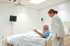 A healthcare worker checks on a patient in a hospital bed. The scene shows a medical setting with a focus on patient care and wellness. Predominant colors are white and blue.