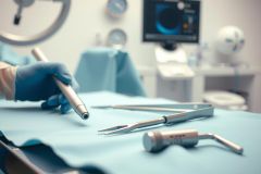 Surgical instruments and a medical device on a blue operating table. A gloved hand is visible in a sterile surgical environment. Focus on precision and medical technology.